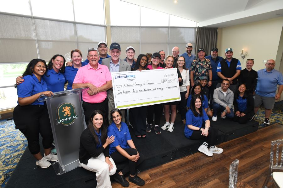 A group of people pose indoors with a large donation check from Extendicare to the Alzheimer Society of Canada at the Lionhead Golf Club.