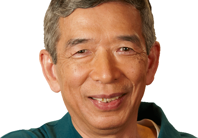 An older man with short gray hair and a teal shirt smiles at the camera against a plain background.