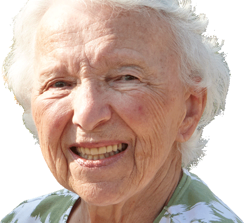 An elderly woman with short white hair is smiling at the camera, wearing a green and white patterned top.