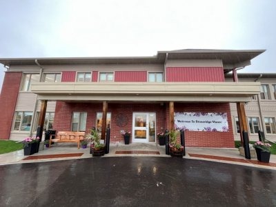 Two-story building with red and beige siding, large entrance, flower pots, and a "Welcome to Knowledge Manor" banner beside the front door on a wet day.