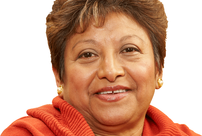 A woman with short brown hair and gold earrings is wearing an orange sweater and smiling at the camera against a plain background.