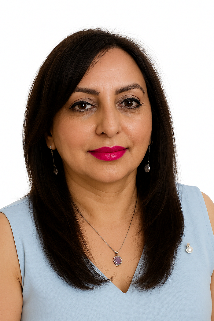 Woman with straight dark hair wearing a light blue sleeveless top, a pendant necklace, drop earrings, and bright pink lipstick, posing against a white background.