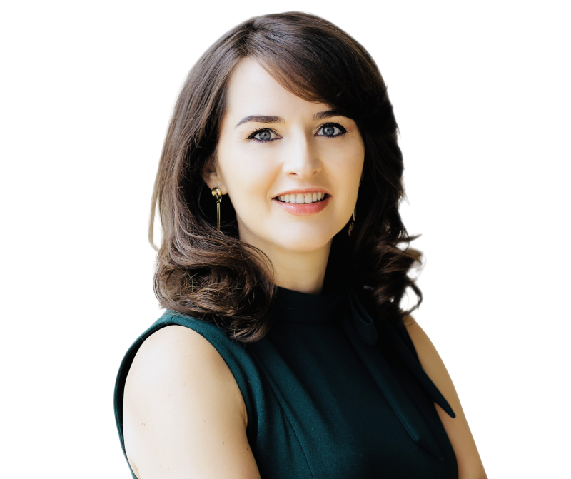 Woman with medium-length brown hair, wearing a sleeveless dark green top, smiling and looking at the camera against a plain white background.