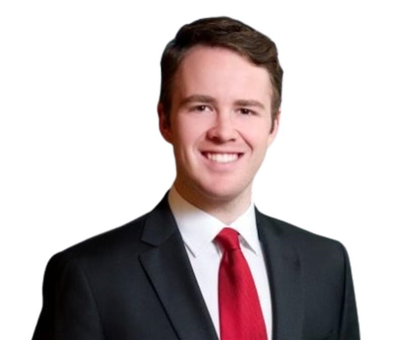 A man in a dark suit, white shirt, and red tie is smiling at the camera against a plain white background.