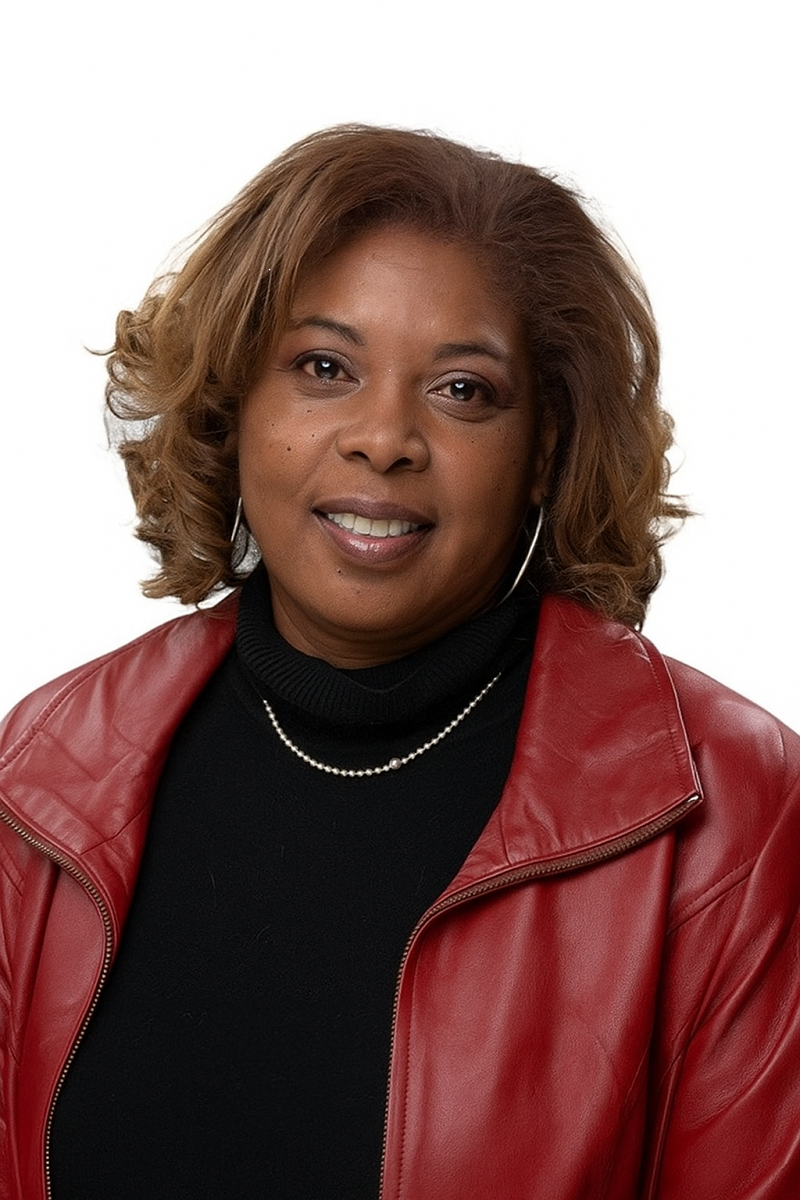 A woman with shoulder-length light brown hair, wearing a red leather jacket, black turtleneck, and pearl necklace, smiles at the camera against a white background.