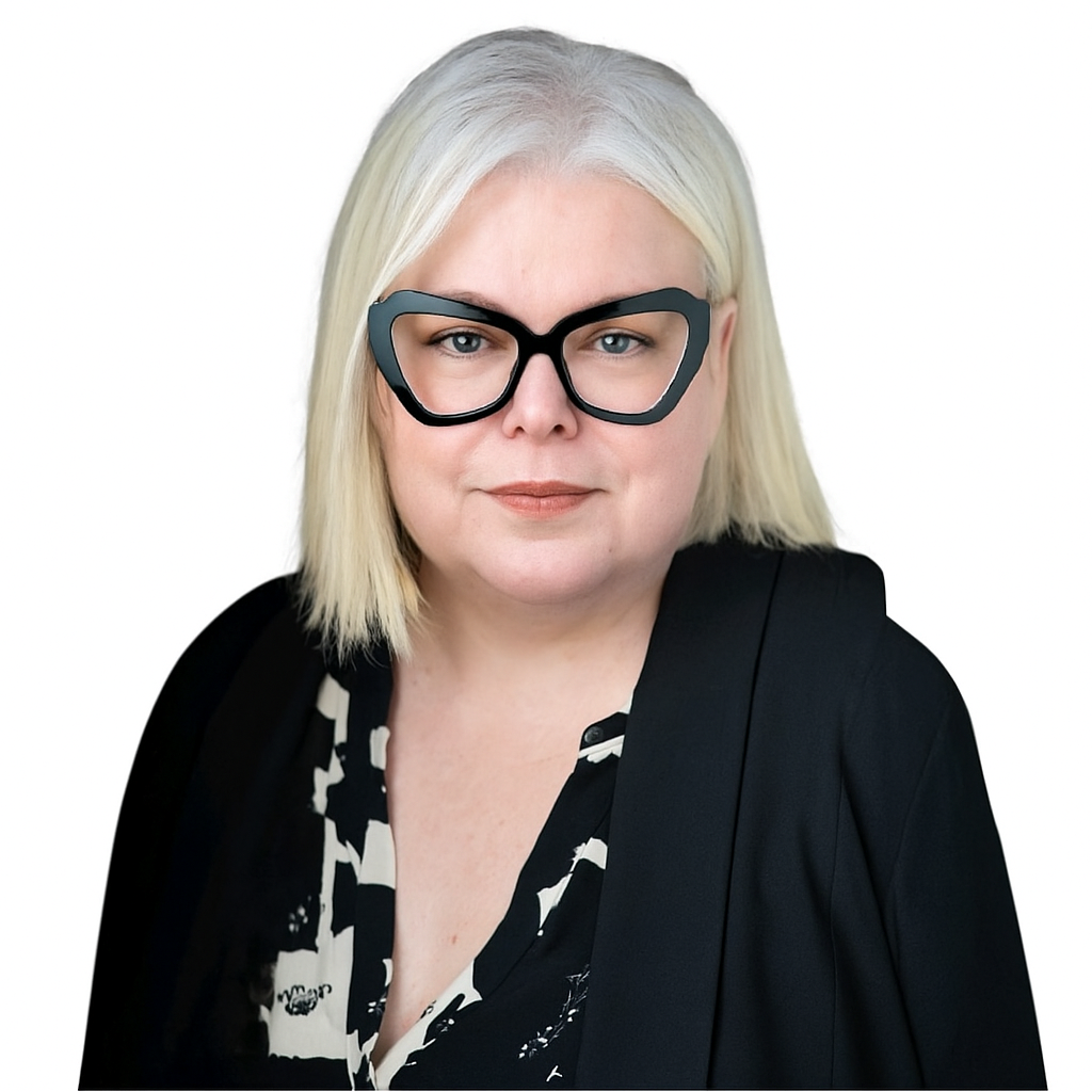 A woman with straight, shoulder-length platinum blonde hair, wearing large black glasses, a black patterned blouse, and a black jacket, poses against a white background.